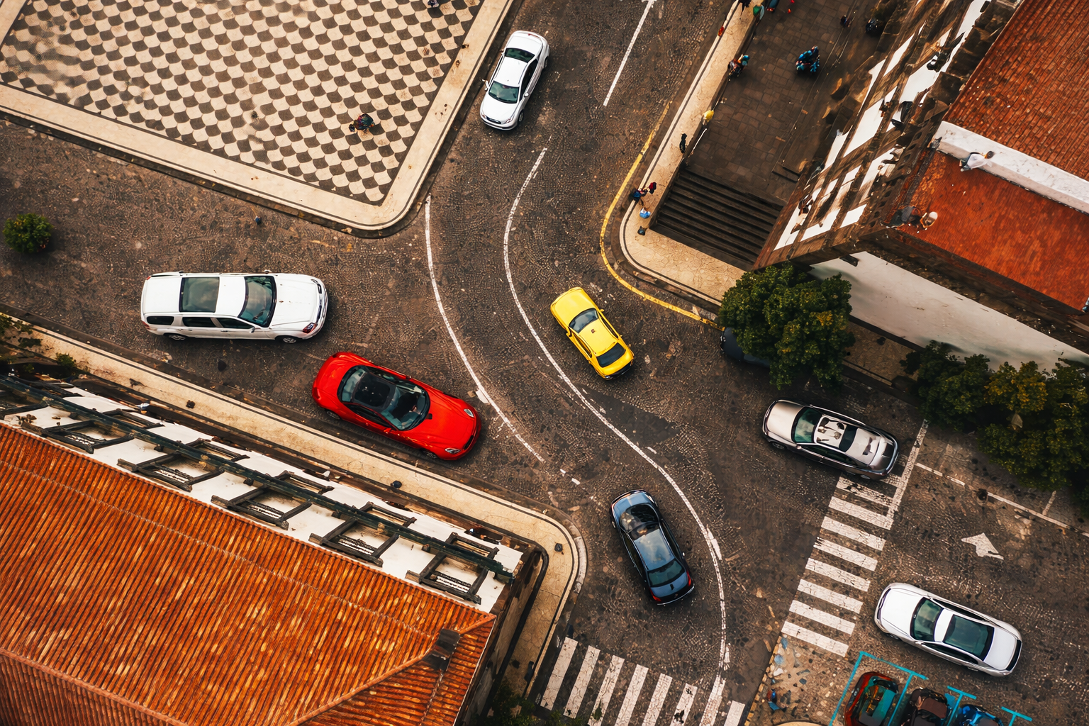 Aerial view of a European city intersection featuring a red Ferrari and yellow taxi, representing luxury inventory for an Auto Broker.